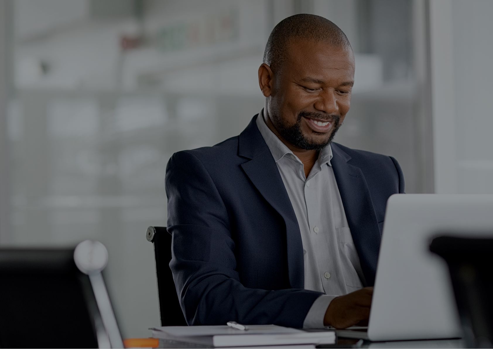 Positive mature businessman working on laptop in modern office  Successful african business man working on computer while sitting at desk  Smiling middle aged man working in a corporate 