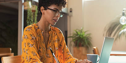 Focused college student sitting in cafeteria taking notes while using laptop  Young brazilian woman doing research for business at coffee shop  African american girl sitting in cafe using computer and writing notes  r