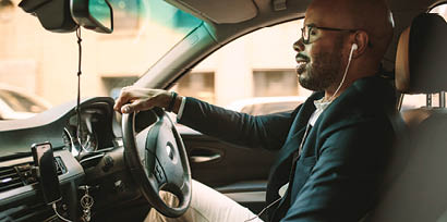 Side view of young man in suit listening music while driving car  African businessman driving a vehicle to office 