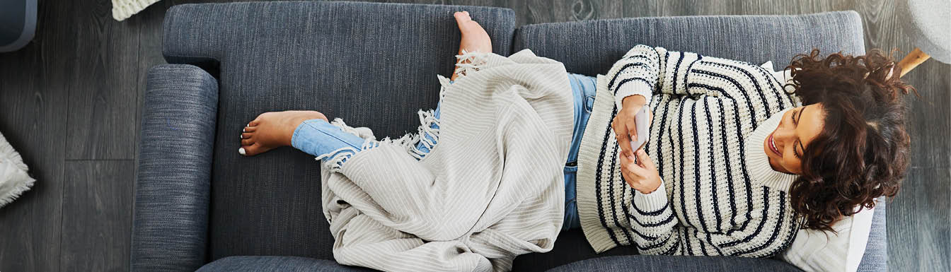 High angle shot of an attractive young woman using her cellphone while relaxing on a couch at home